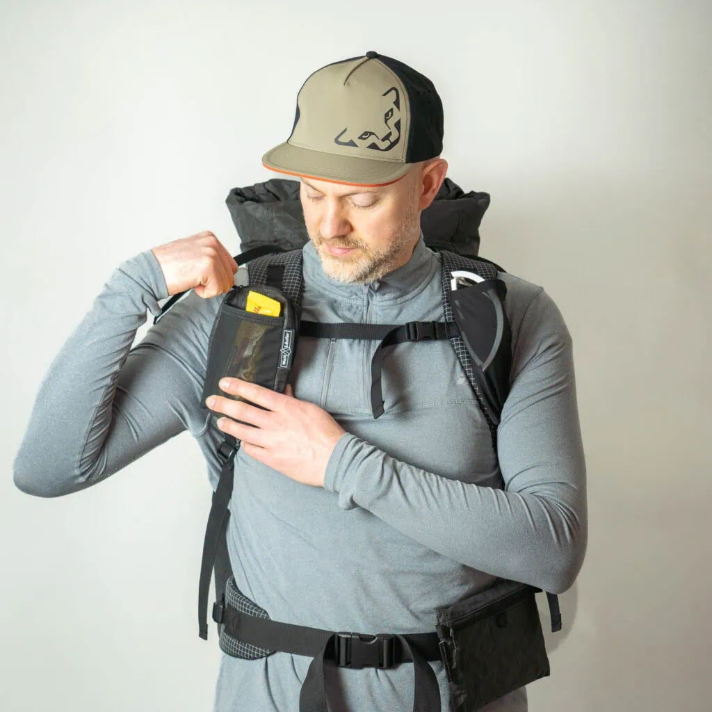 Wanderer greift im Stehen in die Schultergurttasche des Ultraleicht Rucksack Agilist