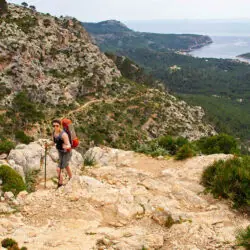 Wanderer mit leichtem Rucksack auf dem GR 221 in der Serra de Tramuntana, Mallorca, mit Küste im Hintergrund.